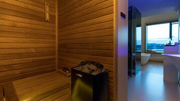 Un sauna moderno con listones de madera en las paredes, un calentador de sauna Harvia y un amplio ventanal con vistas al exterior.