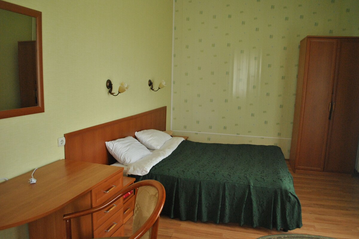 A bedroom with a wooden bed, a desk with drawers, a chair, and a wardrobe.
