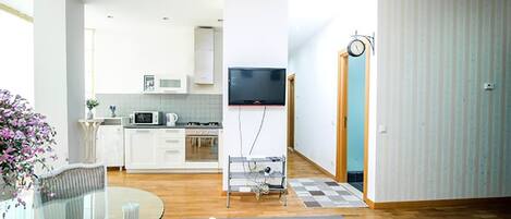 A modern living room with a glass dining table, a sofa, and a TV mounted on the wall.