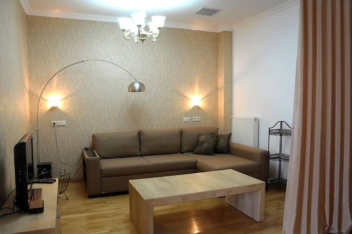 A living room with a brown sofa, a wooden coffee table, and two wall-mounted lamps.