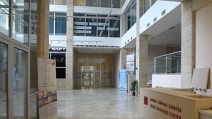 A modern hotel lobby with a reception desk, a directory sign, and a glass elevator. - Rustaveli Besiki Apartments (Tbilisi)