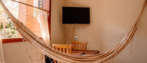 A hammock in a room with a TV mounted on the wall, wooden furniture, and a window with curtains.