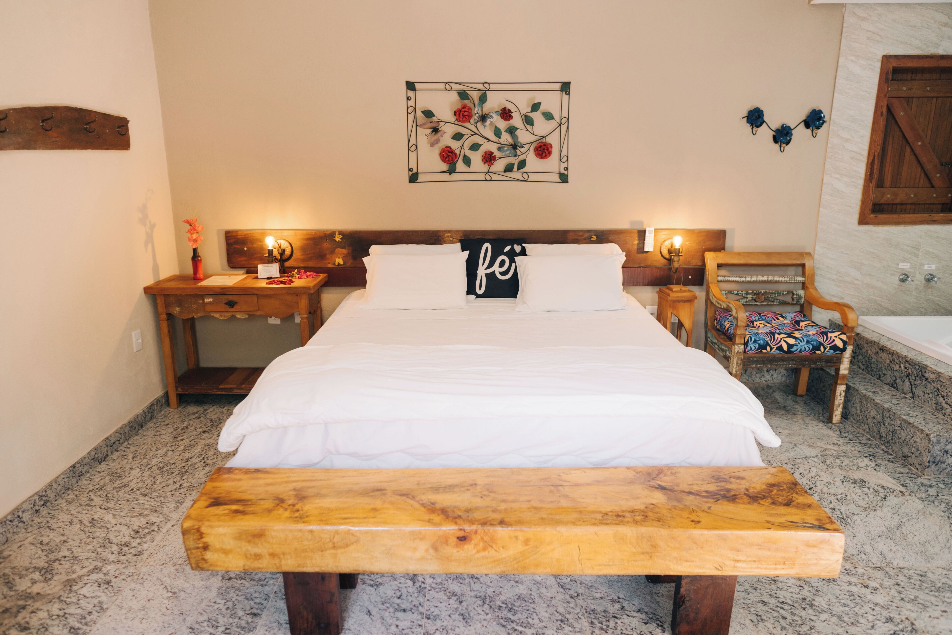 Una camera da letto ordinata con un letto, comodini, una panca, una sedia e un'opera d'arte appesa al muro.