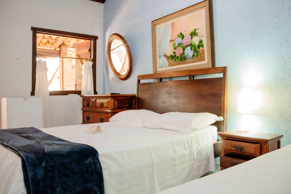 A hotel room with a bed, a dresser, a nightstand, a mirror, and a window with curtains.