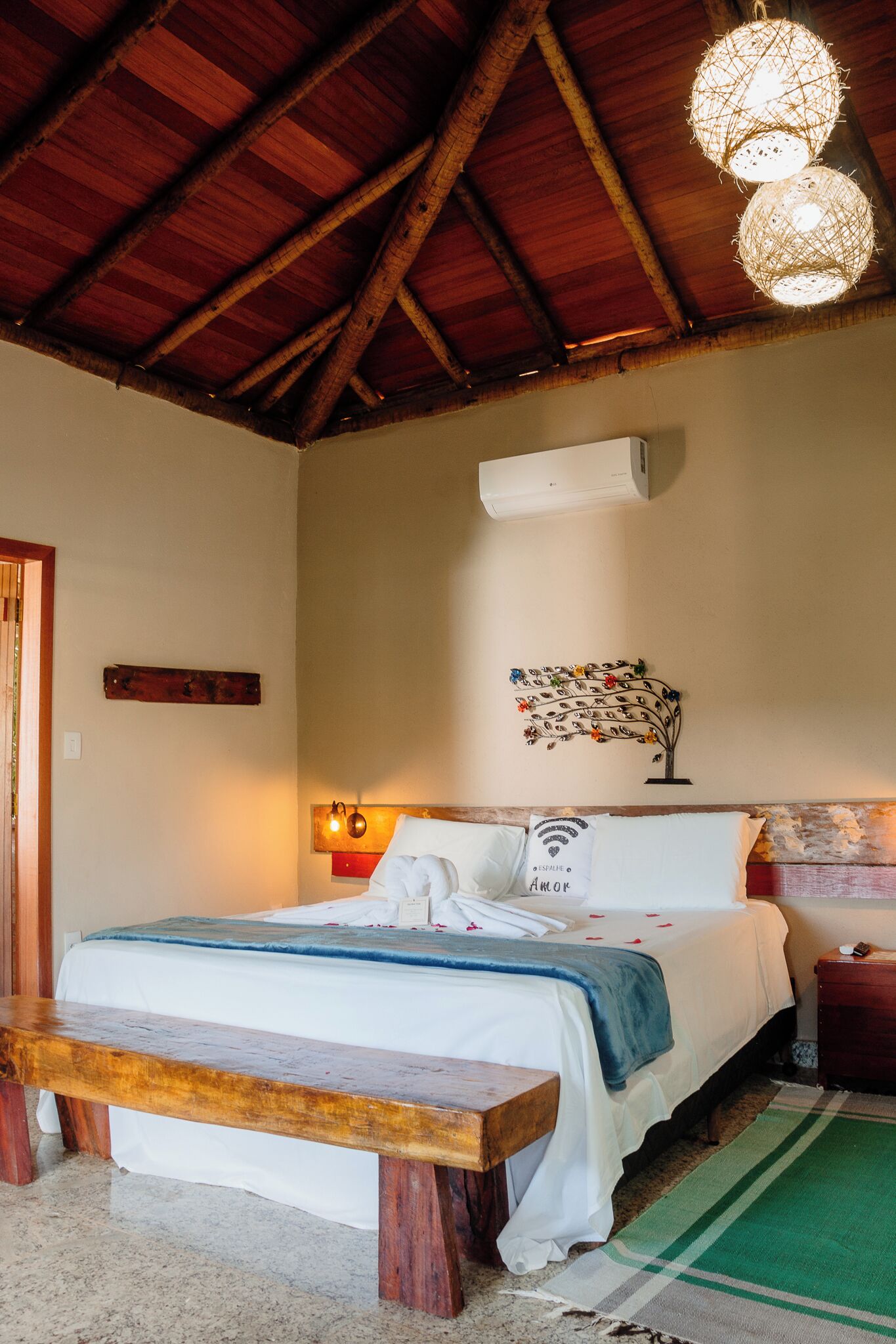 A bedroom with a wooden bed, a bench, a wall-mounted air conditioner, and a decorative metal piece.