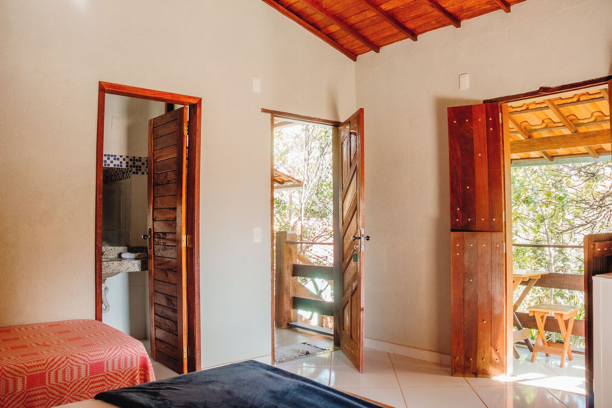 A bedroom with a bed, a wooden door leading to a balcony, and a view of trees outside.