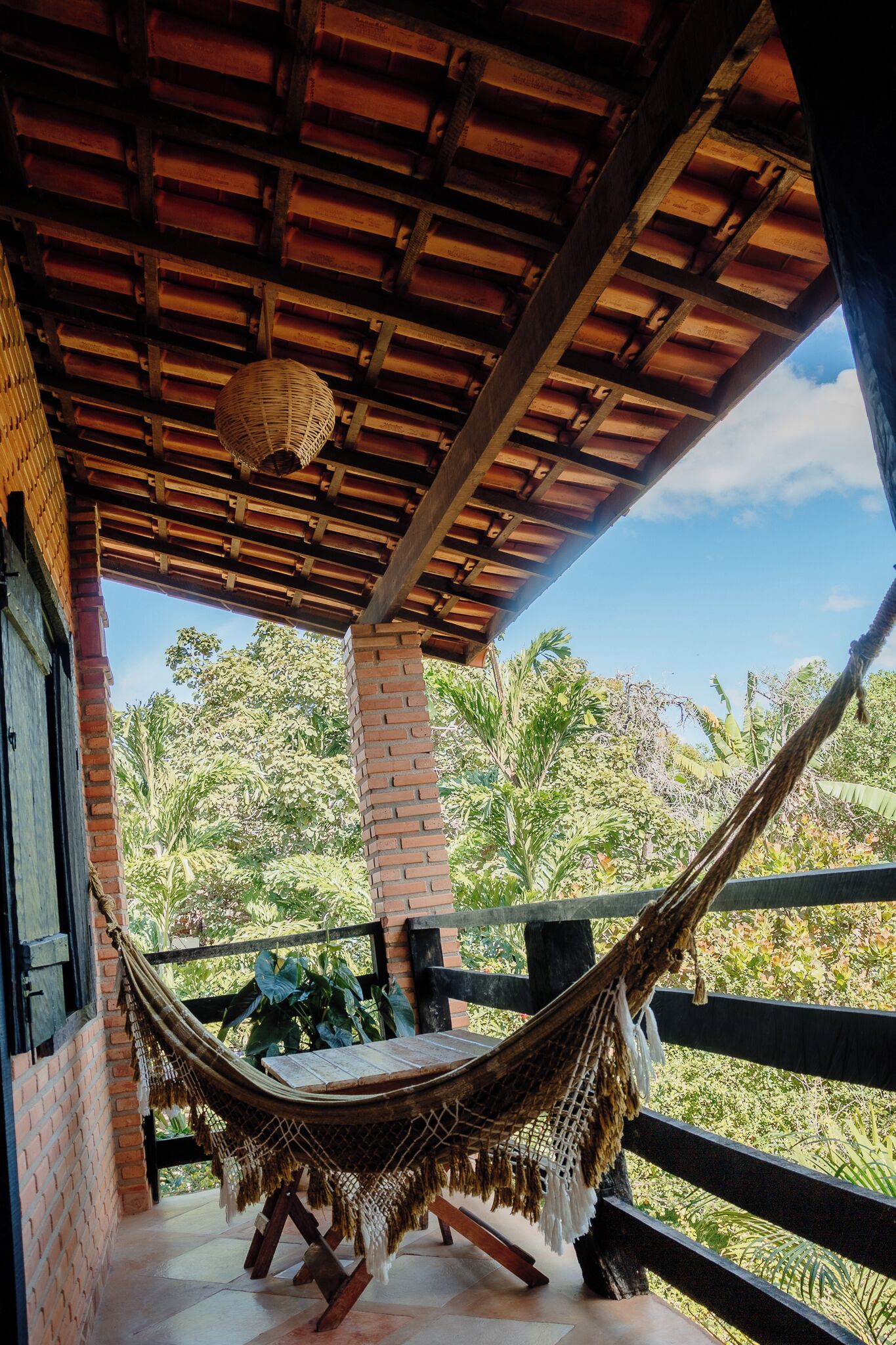A hammock under a wooden roof with a view of lush greenery.