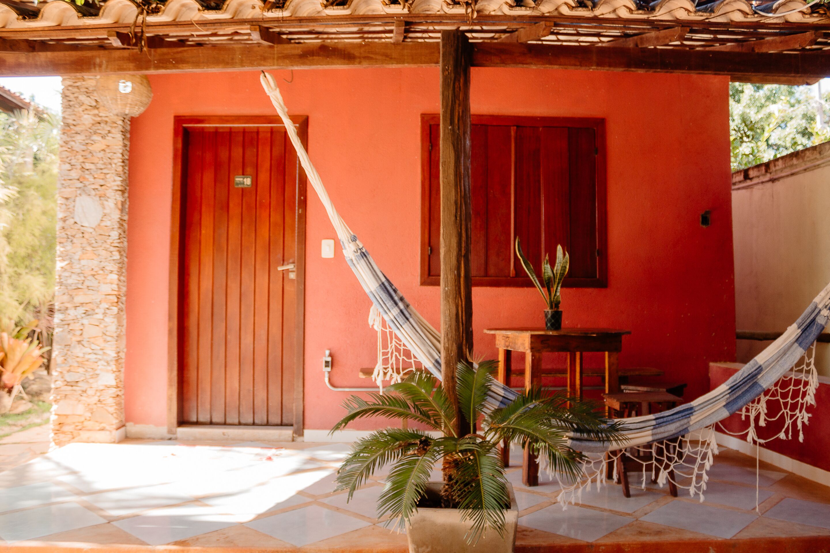 A red building with a wooden door, a hammock, and a potted plant.