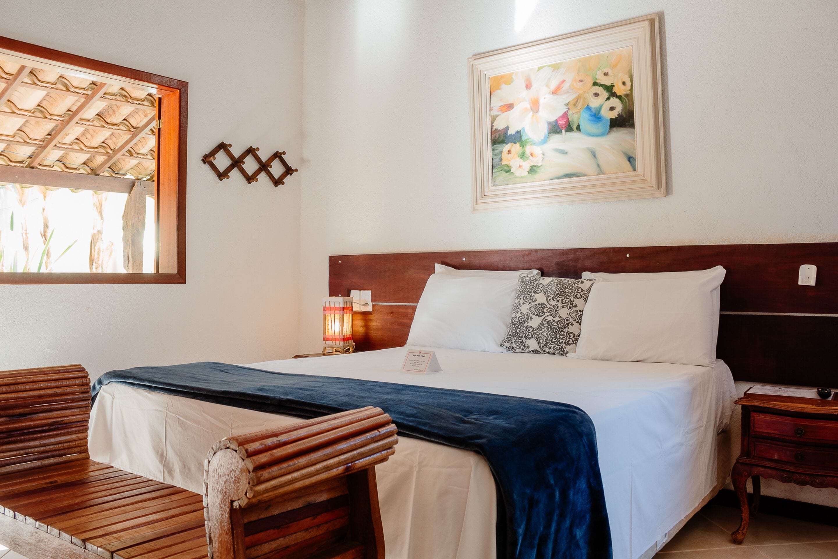 Une chambre d’hôtel bien aménagée, avec un lit, des meubles en bois, un tableau et une fenêtre avec un cadre en bois.