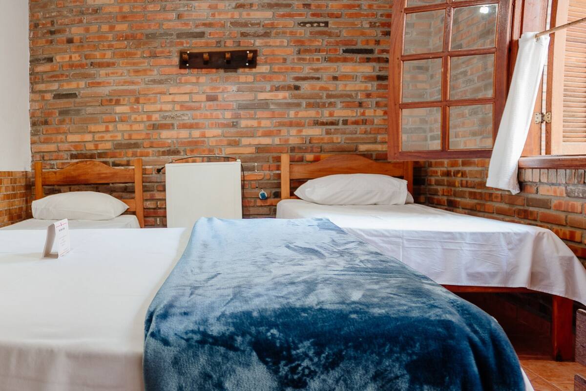 A room with two beds, a brick wall, and a window with shutters.