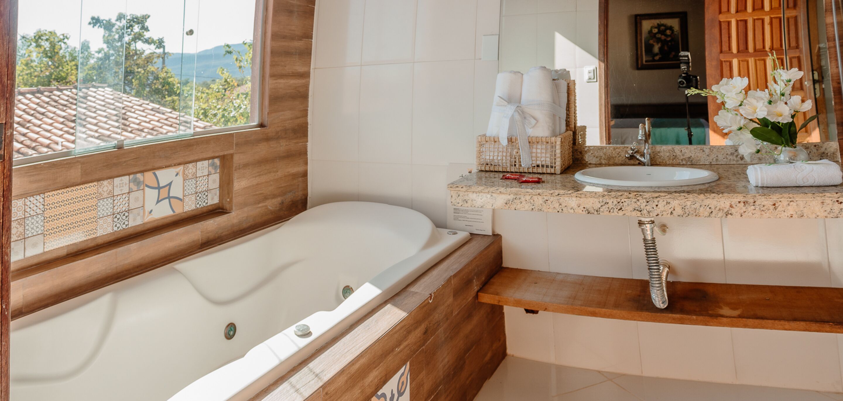 A bathroom with a large bathtub, a wooden vanity, a sink, and a window with a view of the mountains.