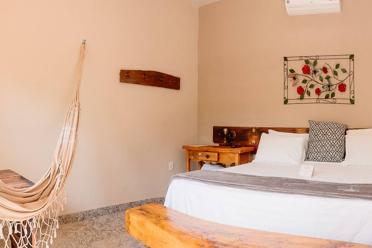A bedroom with a bed, a wooden chair, a TV, a wall decoration, a wooden door, and a bathroom with a bathtub.
