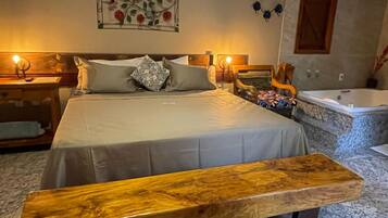 A bedroom with a large bed, a wooden bench, a green area rug, a wall-mounted air conditioning unit, and a bathtub.