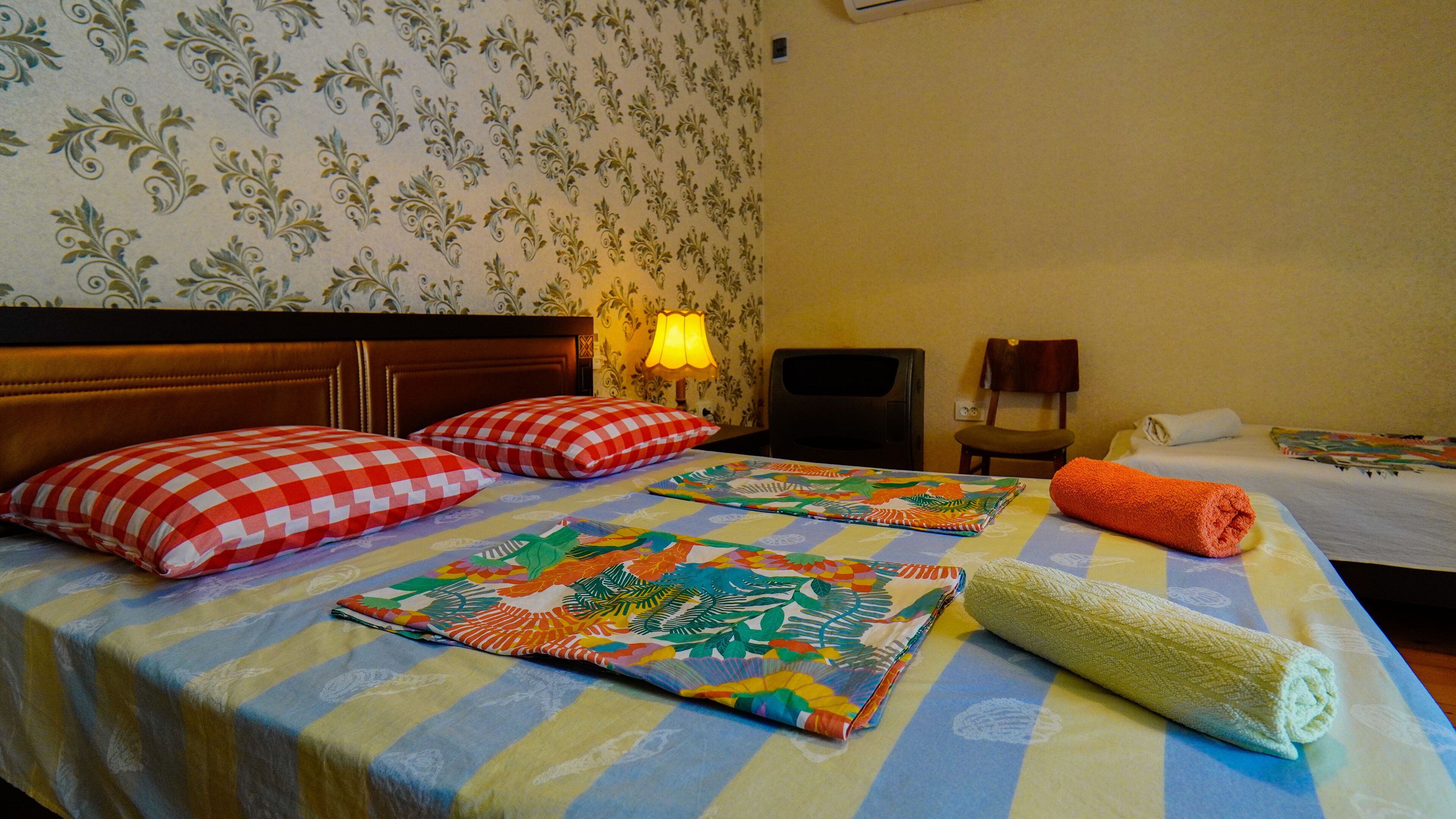 Una habitación de hotel con una cama, dos almohadas, una manta, una toalla enrollada, una lámpara, una silla y un televisor.