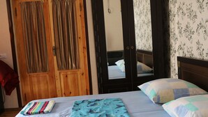 Une chambre à coucher avec un lit, des oreillers et une couverture pliée. On y trouve des portes en bois et un miroir.