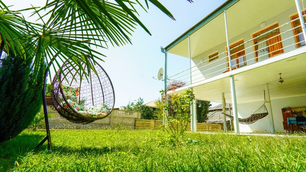 Une maison à deux étages avec un balcon, un fauteuil suspendu et un jardin.