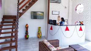 A reception area with a wooden staircase, a TV, and a receptionist. - Hotel Pousada WS (Ipojuca)