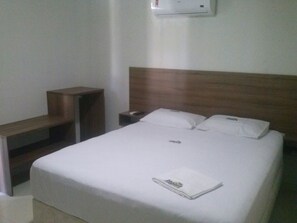 A hotel room with a single bed, a nightstand, a wooden bench, and a wall-mounted air conditioner. - Hotel Pousada WS (Ipojuca)