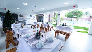 A dining area with tables set for a meal, a Christmas tree, and a view of a swimming pool. - Hotel Pousada WS (Ipojuca)