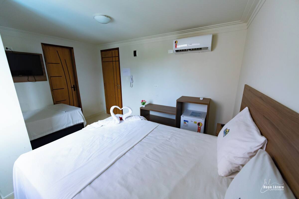 Habitación de hotel con cama, un escritorio pequeño, equipo de aire acondicionado y televisor montado en la pared.