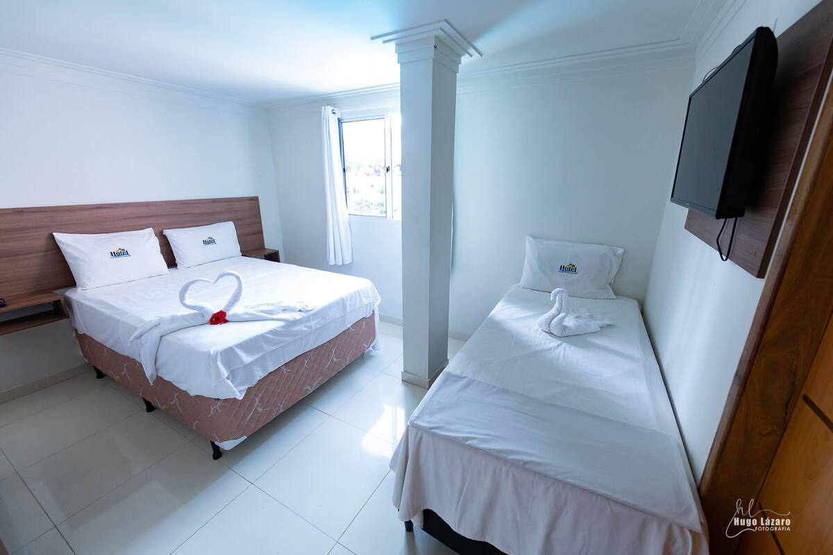 Habitación de hotel con dos camas, cada una adornada con toallas dispuestas en forma de corazón, ropa de cama blanca y cabeceros de madera.