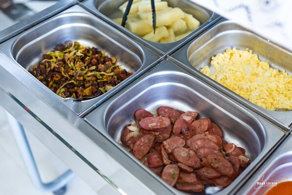 A buffet with various food options including sausages, scrambled eggs, and potatoes.