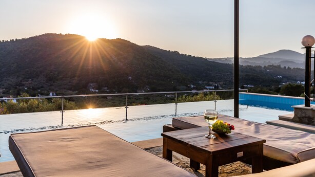 A rooftop terrace with a pool, wooden furniture, and a glass of wine.
