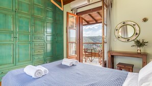 A bedroom with a bed, a wooden ceiling, a green wardrobe, and a balcony with a view.