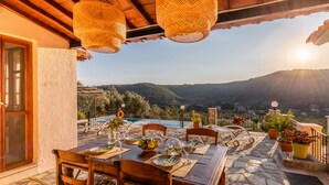 An outdoor dining area with a stone floor, wooden tables and chairs, and hanging wicker lamps.