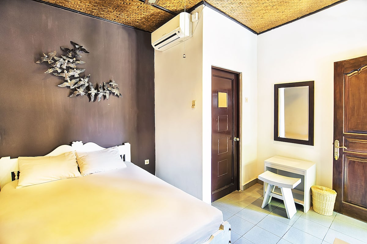 A bedroom with a bed, a small bedside table, a mirror, and an air conditioning unit.