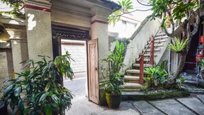 A courtyard with a wooden door, potted plants, and a staircase. - Puri Agung Homestay (Kuta)