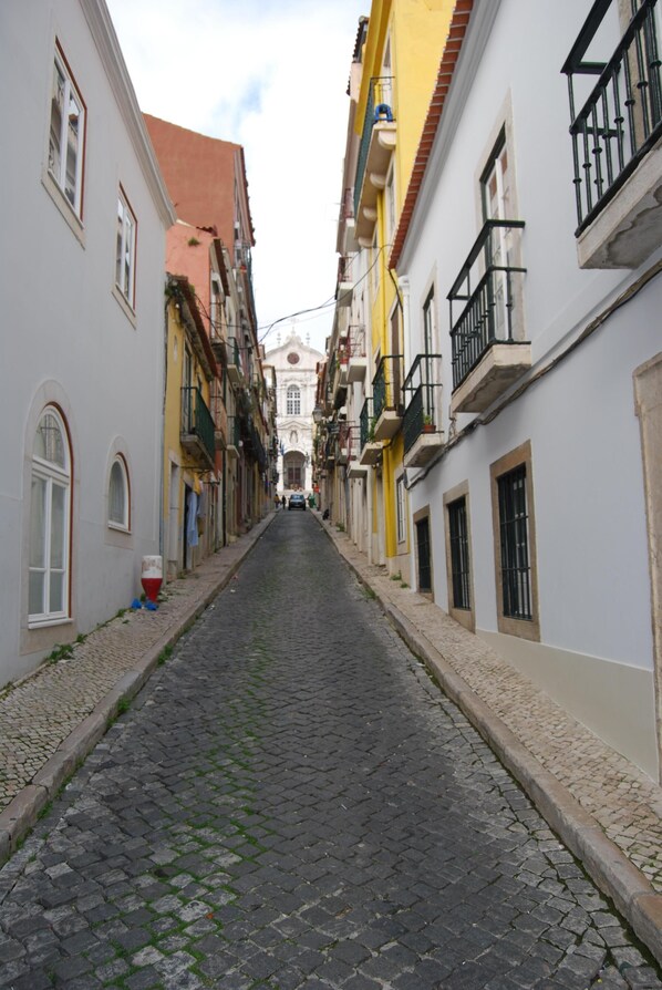 Uma rua de paralelepípedos estreita, ladeada por edifícios com sacadas e janelas em arco.