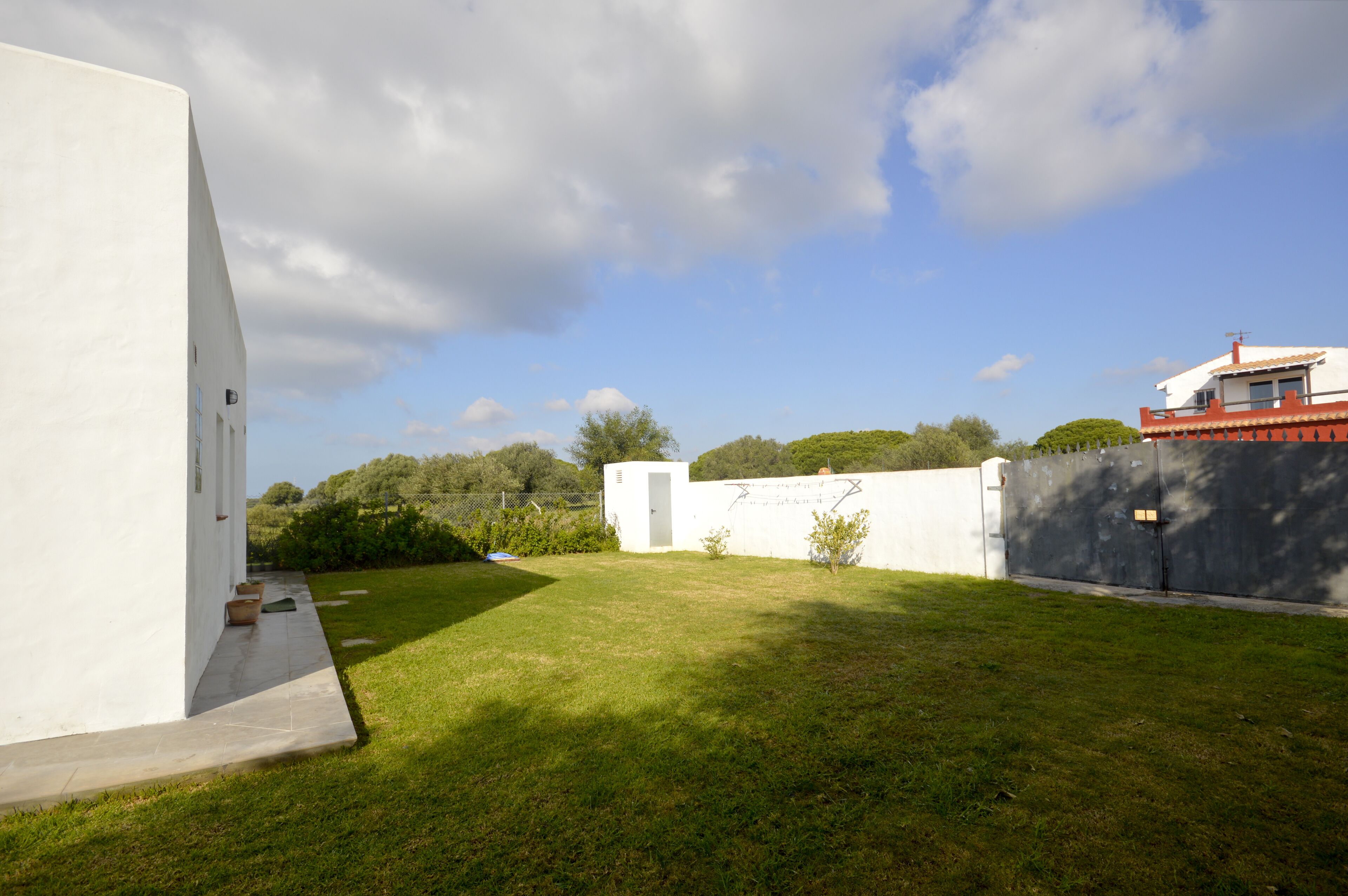 A modern building with a white exterior, a small garden area, and a clear sky.