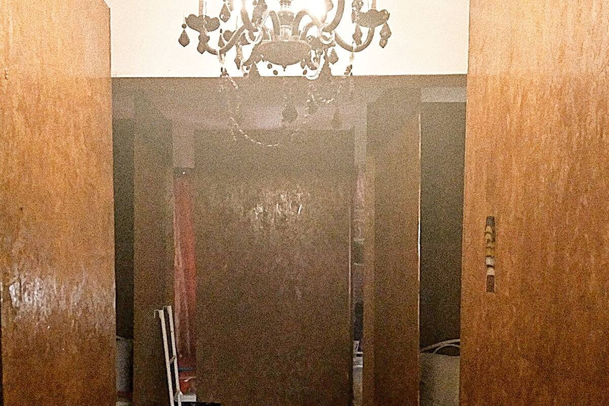 A narrow hallway with wooden flooring, a chandelier, and a ladder leaning against the wall.