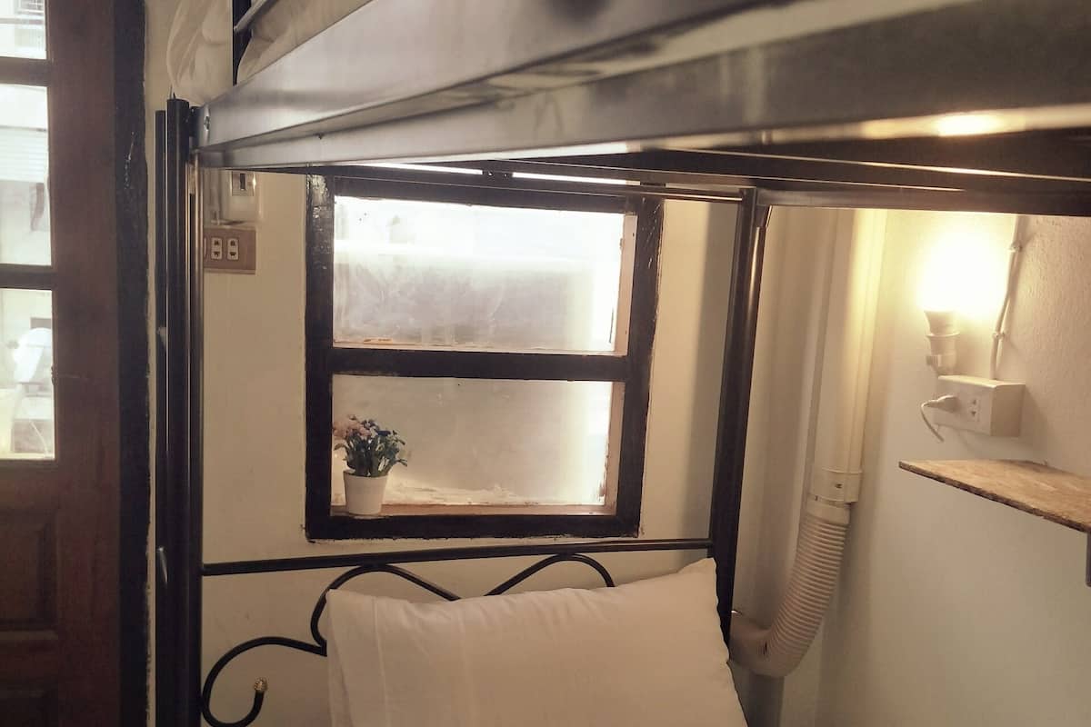 A bunk bed with a window, a bedside table with a lamp, and a small shelf with a plant.