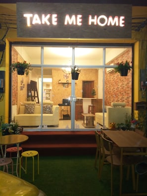 A restaurant with a neon sign reading "TAKE ME HOME". Inside, there are multiple seating areas with tables and chairs.