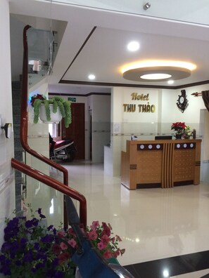 Un hall d’accueil d’hôtel avec un comptoir en bois, une horloge et une enseigne indiquant « Hôtel Thu Thao ».