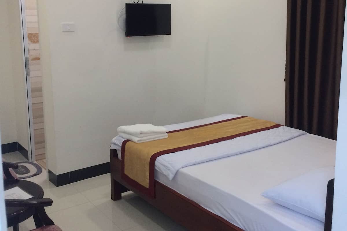 Habitación de hotel con cama, televisor montado en la pared, escritorio y silla.