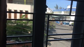 A view through a window with a metal grid, featuring a street with buildings, a parked car, and some greenery. - Hotel Thu Thao (Phan Rang)