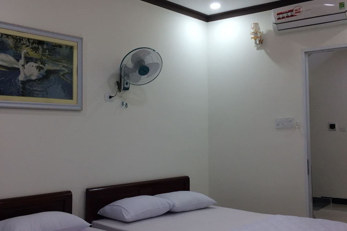 Habitación de hotel con dos camas individuales, ventilador de techo, unidad de aire acondicionado y un cuadro en la pared.