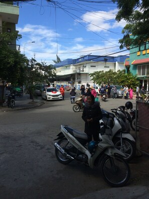 Une scène de rue avec des motos et des voitures garées, des bâtiments et des passants.