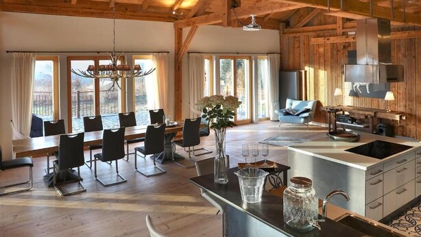Amplia sala de estar con techo de madera, una mesa de comedor con sillas, una isla de cocina y un ventanal con vistas al exterior.
