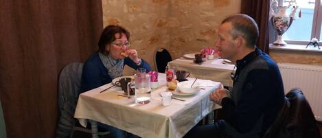 Comedor con paredes de piedra, una mesa dispuesta con platos, tazas y cubiertos.