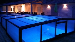 A swimming pool with a glass enclosure, a covered seating area, and a building with a garage. - Near Soulac-sur-Mer, 6-bedroom villa with heated indoor pool, jacuzzi, and sauna (Grayan-Et-L'hôpital)