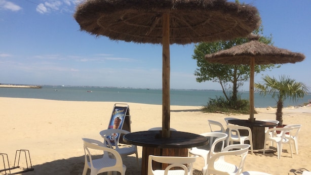 A beachside café with white plastic chairs and tables, two thatched umbrellas, and a menu board. - Near Soulac-sur-Mer, 6-bedroom villa with heated indoor pool, jacuzzi, and sauna (Grayan-Et-L'hôpital)