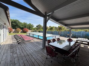 Une terrasse extérieure couverte avec une piscine, une table à manger avec des chaises et une plateforme en bois.