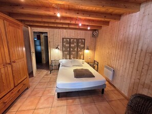Une pièce aux murs lambrissés, comprenant un lit, deux tables de chevet, un radiateur et une porte donnant sur une autre pièce.