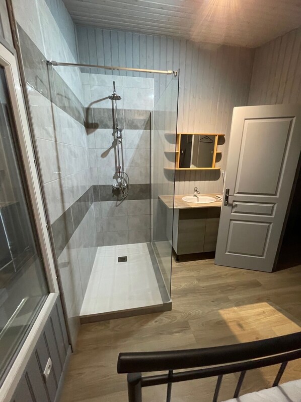 A modern bathroom with a glass-enclosed shower, a wooden vanity with a mirror, and a door.