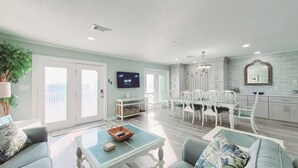 A spacious living room with a dining area, a kitchen with white cabinets, and a mounted TV.