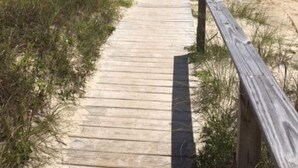 A wooden boardwalk leading to a beach with a clear view of the ocean.